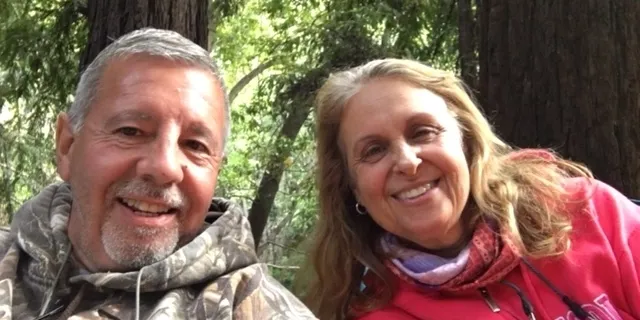 Smiling couple enjoying a moment outdoors with greenery in the background.