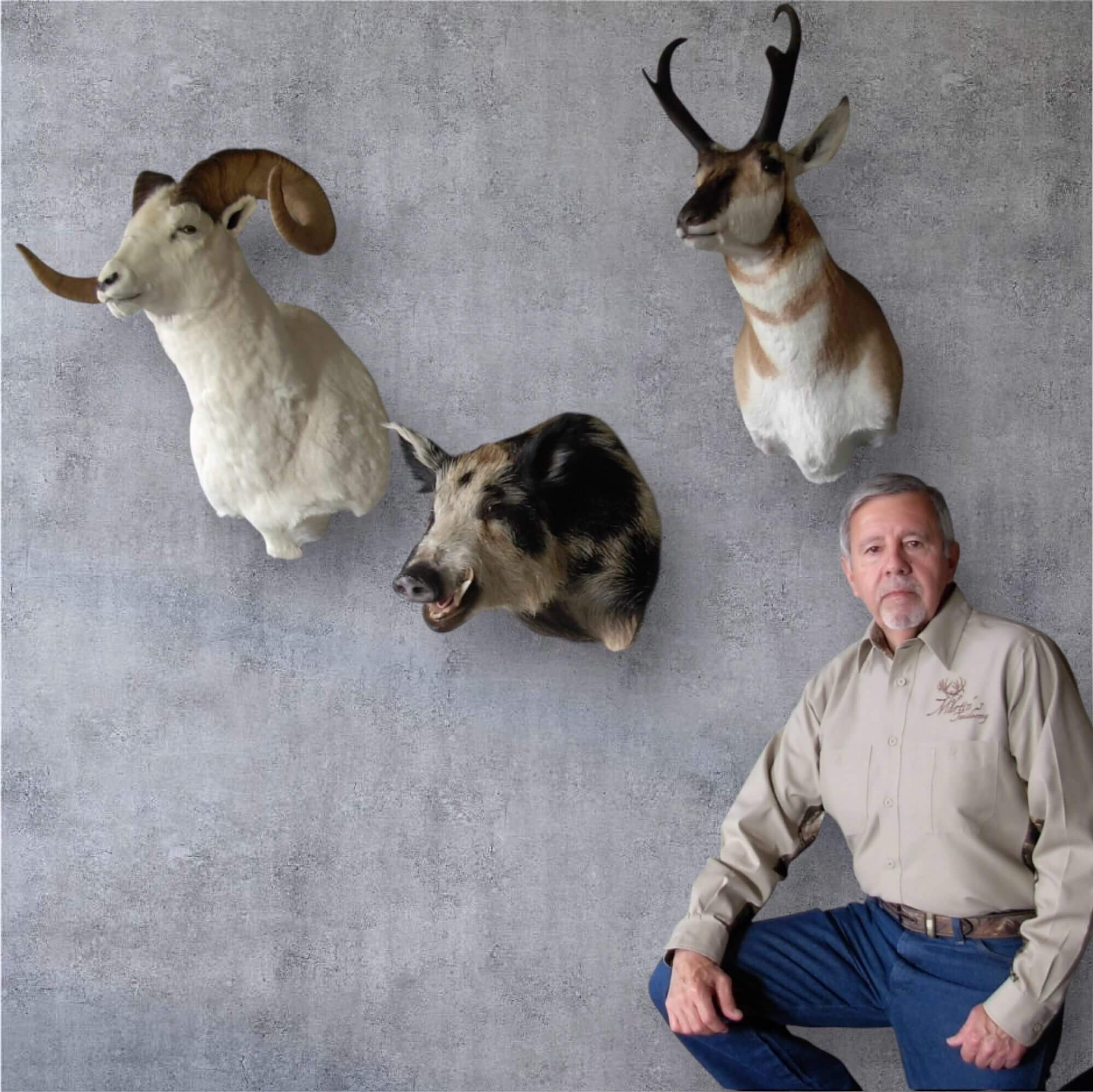 A man poses beside mounted animal heads on a wall.